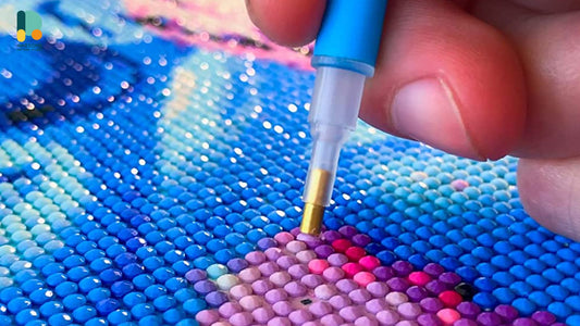 Close-up of a hand using a diamond pen to place colorful drills on a diamond painting canvas, showcasing the intricate detail and hands-on aspect of the craft.